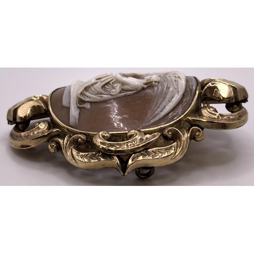 534 - A late 19th/early 20th century oval shell cameo brooch, decorated a lady, in a yellow metal scrolled... 