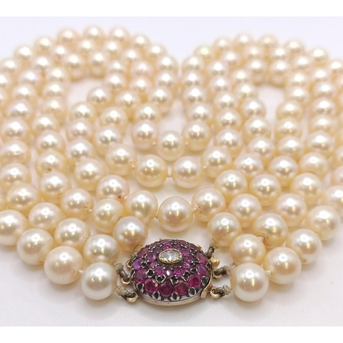 558 - A triple strand cultured pearl necklace, with a yellow metal, red and white stone clasp