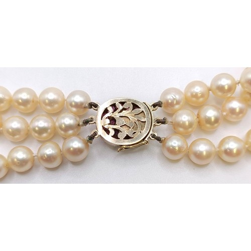 558 - A triple strand cultured pearl necklace, with a yellow metal, red and white stone clasp