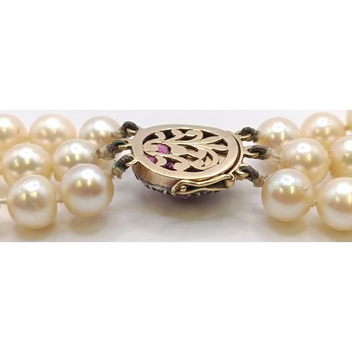 558 - A triple strand cultured pearl necklace, with a yellow metal, red and white stone clasp