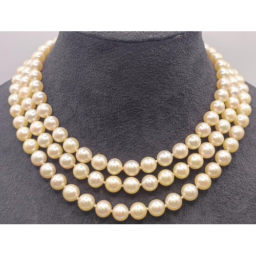 558 - A triple strand cultured pearl necklace, with a yellow metal, red and white stone clasp