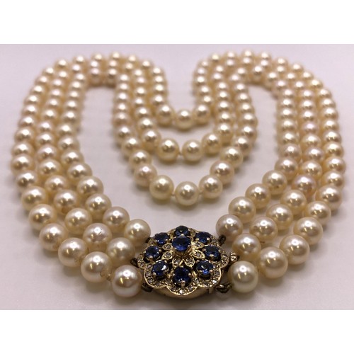 673 - An Akoya cultured pearl triple strand necklace, the clasp set with cornflower blue sapphires