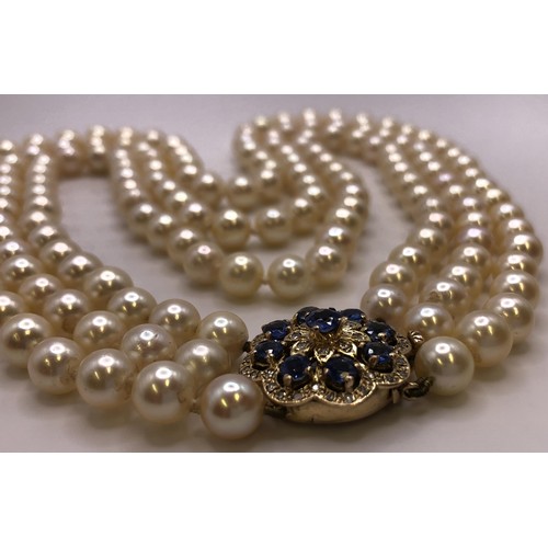 673 - An Akoya cultured pearl triple strand necklace, the clasp set with cornflower blue sapphires