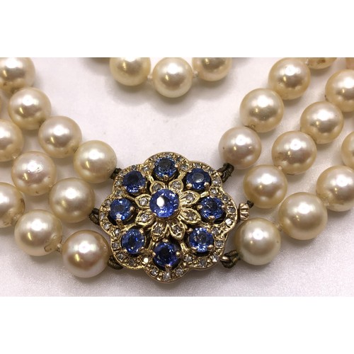 673 - An Akoya cultured pearl triple strand necklace, the clasp set with cornflower blue sapphires