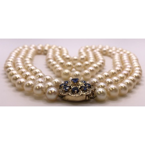 673 - An Akoya cultured pearl triple strand necklace, the clasp set with cornflower blue sapphires