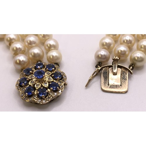 673 - An Akoya cultured pearl triple strand necklace, the clasp set with cornflower blue sapphires