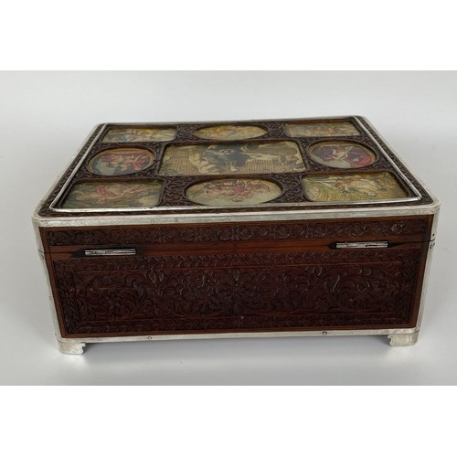 1060 - An Eastern carved wood box, the top inset with prints, with silver coloured metal mounts, 23 cm wide