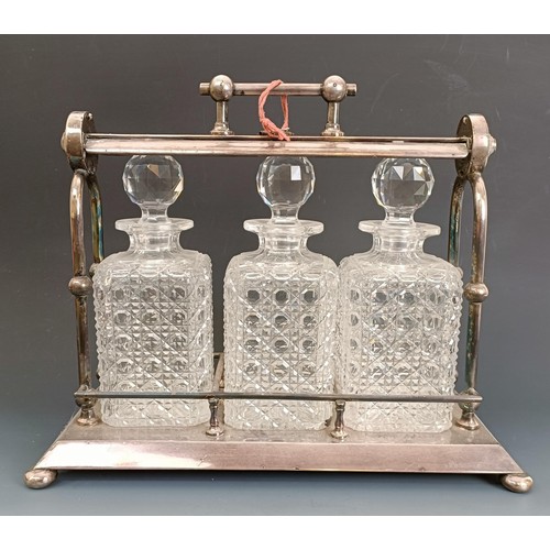 560 - A silver plated three bottle tantalus, with a Dr Christopher Dresser style handle, on bun feet, 39 c... 