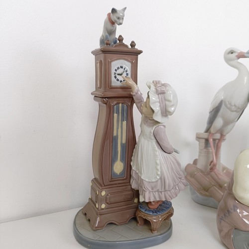 596 - A Lladro figure of a girl cleaning a longcase clock, with a cat on top of the clock, two other Lladr... 