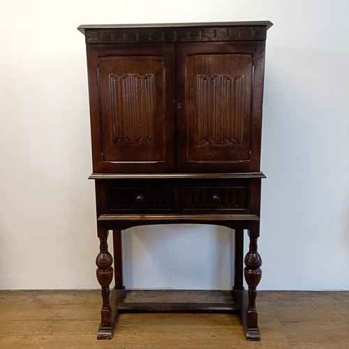 927 - An oak cupboard on stand, having a pair of linen fold panel doors above a drawer, 77 cm wide