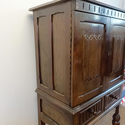 927 - An oak cupboard on stand, having a pair of linen fold panel doors above a drawer, 77 cm wide