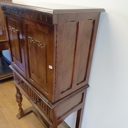 927 - An oak cupboard on stand, having a pair of linen fold panel doors above a drawer, 77 cm wide