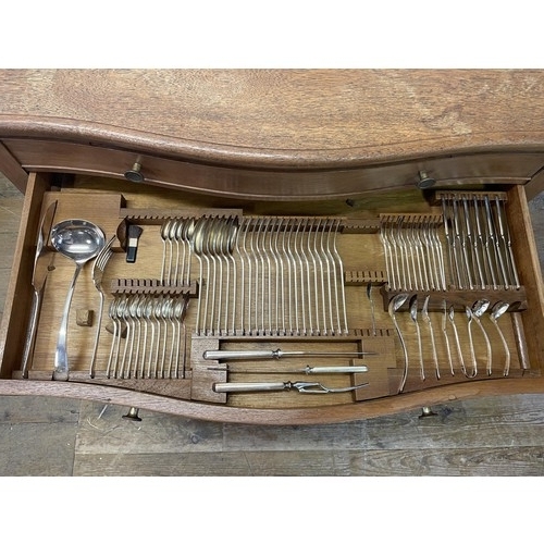 975 - A silver plated canteen of cutlery, settings for twelve, in an oak serpentine two drawer table, 97 c... 