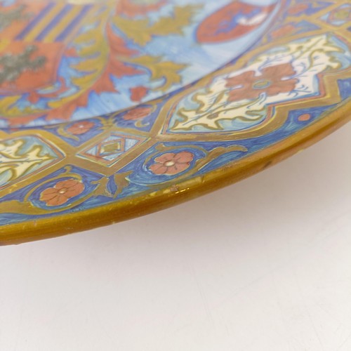 824 - A majolica charger, decorated crest, with a floral border, signed verso, 40 cm diameter