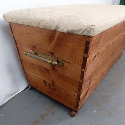 25 - A pine ottoman, with an upholstered top and brass handles, 124 cm wide