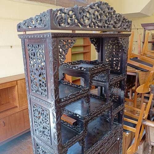 876 - A Chinese hardwood cabinet, the top with stepped shelves, on a base with two cupboard doors, profuse... 