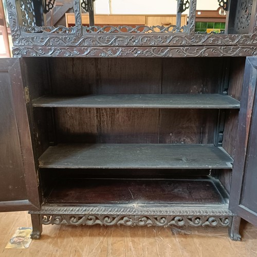 876 - A Chinese hardwood cabinet, the top with stepped shelves, on a base with two cupboard doors, profuse... 