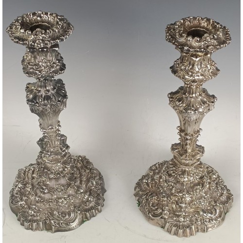 16 - A pair of George IV silver candlesticks, crested, decorated in high relief flowers and foliage, ...