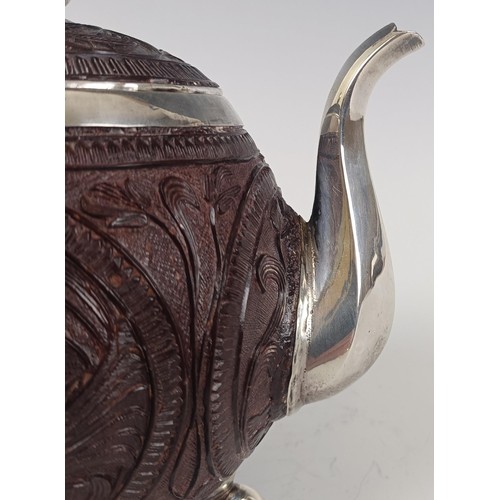 52 - An Indian coconut teapot and cover, with silver coloured metal mounts and carved decoration, on thre... 