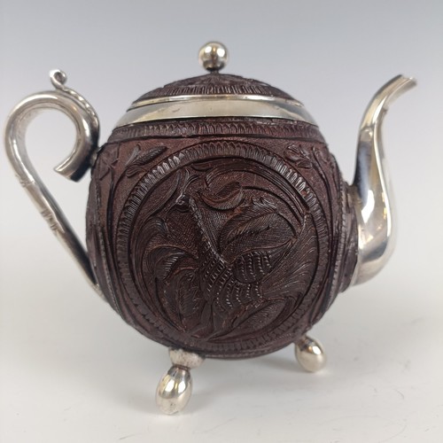 52 - An Indian coconut teapot and cover, with silver coloured metal mounts and carved decoration, on thre... 