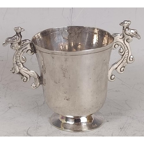 82 - An 18th century silver coloured metal small two handled cup, the handles decorated birds, 7 cm high