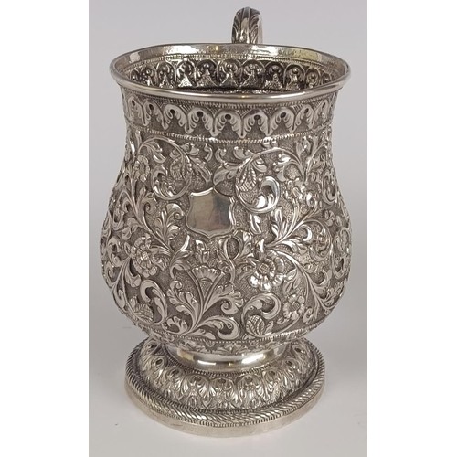 130 - A 19th century Indian silver coloured metal mug, embossed flowers and foliage, 12.5 cm high