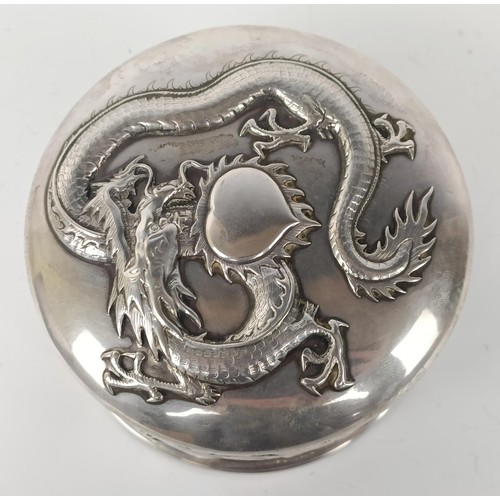 1011 - A Chinese silver coloured metal box, decorated a  dragon, 10 cm diameter...