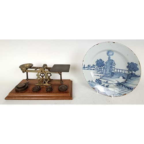 1114 - A Delft plate, decorated a mill by a bridge, 22 cm diameter, and a set of brass postal scales (2)