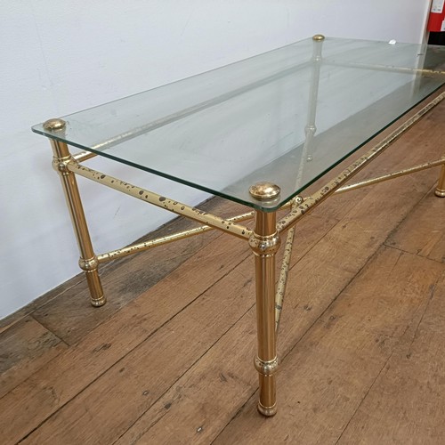 689 - A glass topped coffee table, on a brass base, 113 cm wide