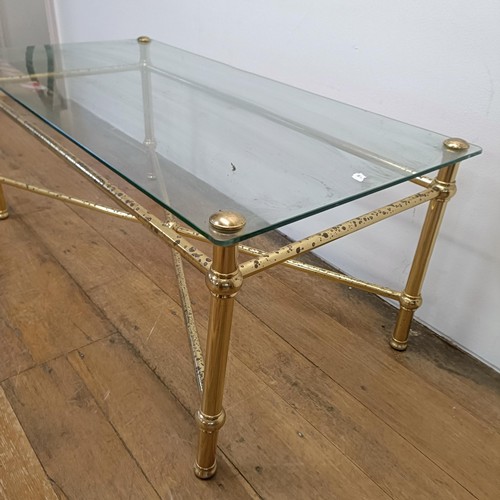 689 - A glass topped coffee table, on a brass base, 113 cm wide