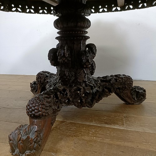 755 - A carved Burmese centre table, with a carved and pierced frieze, to a column support to a triangular... 