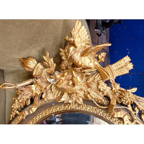 813 - A gilt gesso overmantel oval mirror, the finial in the form of nesting birds, 135 x 80 cm