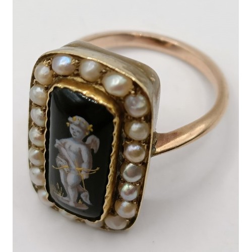 701 - A mourning ring, with black enamel plaque, decorated putti, surrounded by seed pearls, ring size N