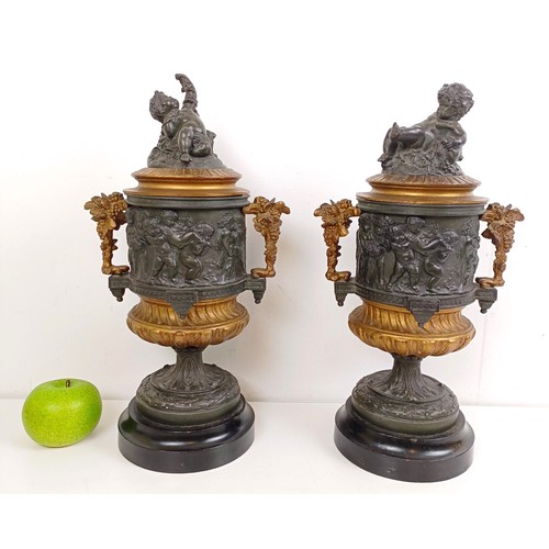 1080 - A pair of brass and bronze urns, with covers, with cherub finials on wooden bases, 40 cm high (2)