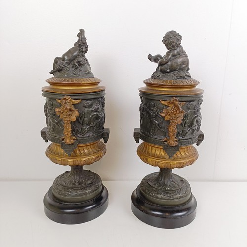 1080 - A pair of brass and bronze urns, with covers, with cherub finials on wooden bases, 40 cm high (2)