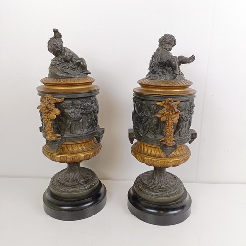 1080 - A pair of brass and bronze urns, with covers, with cherub finials on wooden bases, 40 cm high (2)