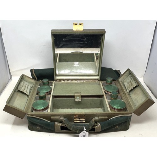 988 - An Art Deco travelling dressing case, the glass jars with enamel decoration, in a green leather trav... 