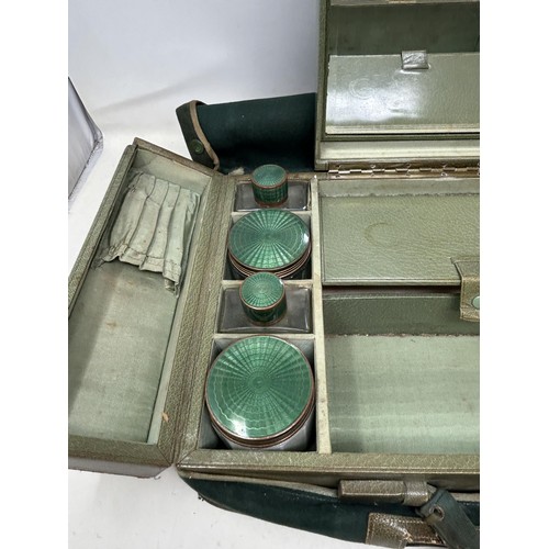 844 - An Art Deco travelling dressing case, the glass jars with enamel decoration, in a green leather trav... 