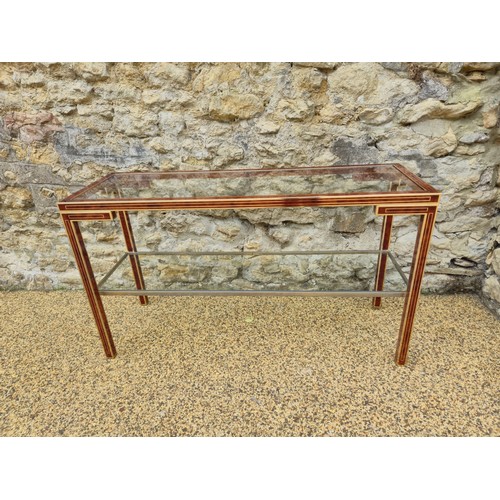 1015 - A brass and lacquered two tier table, with a glass shelf, 128 cm wide