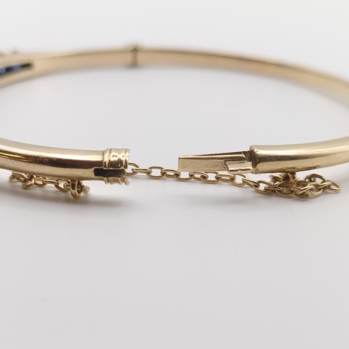 644 - A yellow coloured metal hinged bangle, set fifteen sapphires, graduating from the centre