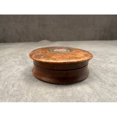 26 - A small, round burl wood box featuring a lift-off lid. The lid is adorned with a central circular me... 