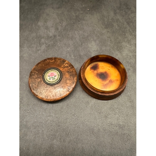 26 - A small, round burl wood box featuring a lift-off lid. The lid is adorned with a central circular me... 