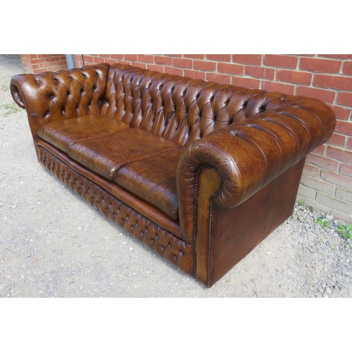 728 - A vintage three seater Chesterfield sofa upholstered in distressed chestnut brown leather, raised on... 