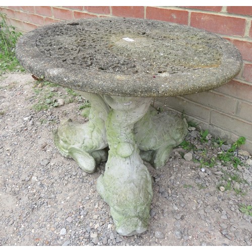 848 - A small circular reconstituted stone garden table with carved top, raised on three moulded fish/drag... 