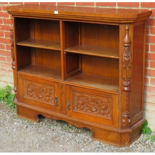 782 - A vintage carved oak low open bookcase comprising four shelves over a cupboard base flanked by a pai... 