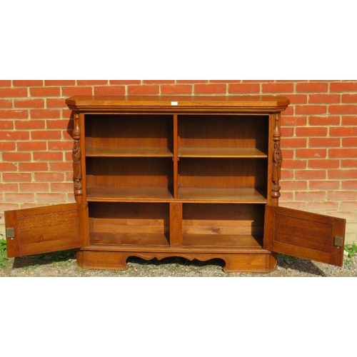 782 - A vintage carved oak low open bookcase comprising four shelves over a cupboard base flanked by a pai... 