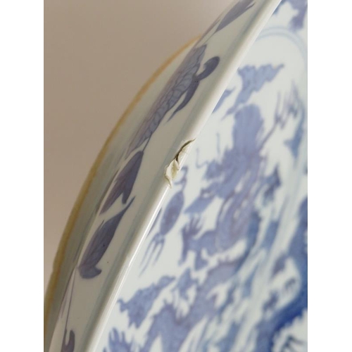 15 - An antique Chinese porcelain blue and white charger depicting a pearl chasing dragon within a four d... 