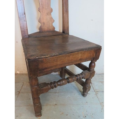 709 - An early 18th century oak hall chair of immense character featuring a shaped back splat, raised on t... 