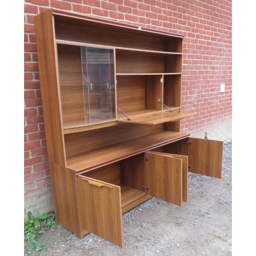 731 - A mid century teak effect wall unit, comprising asymmetrical display shelving with drop down central... 