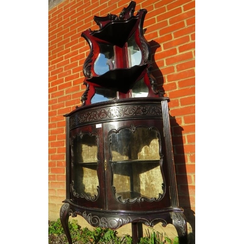 820 - A turn of the century ebonised corner display unit in the Flemish taste, with mirror backed shelves ... 